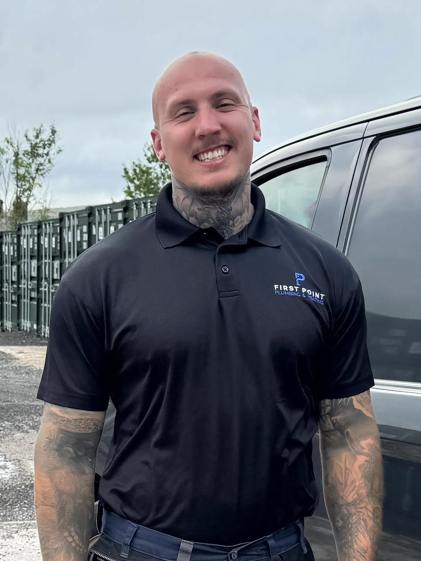 A First Point engineer in a black branded polo standing beside a dark grey van in a yard.