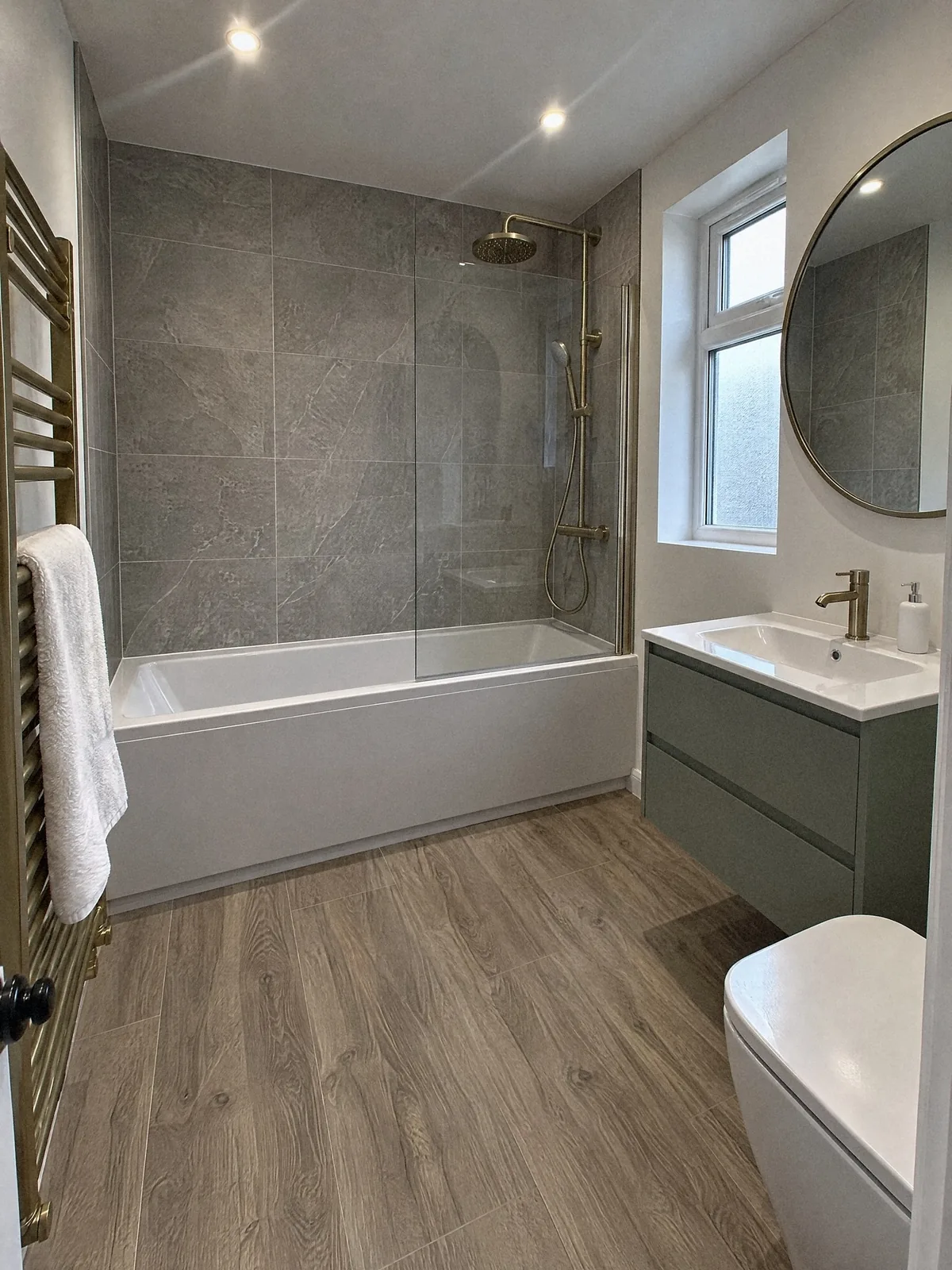 Illustration of a finished bathroom with a brushed brass shower over the bath, a sage green vanity unit and a brass towel radiator