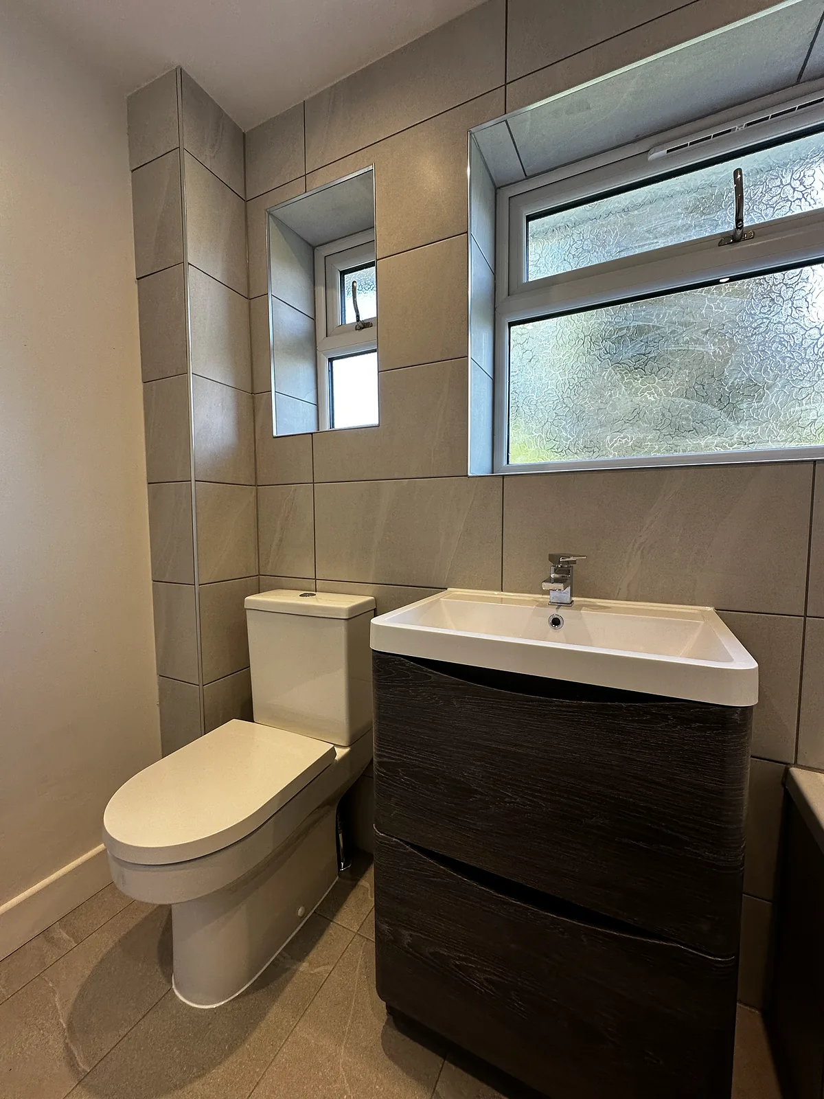 Shower room with stone-effect tiles, a dark wood vanity unit and a close-coupled toilet under a frosted window