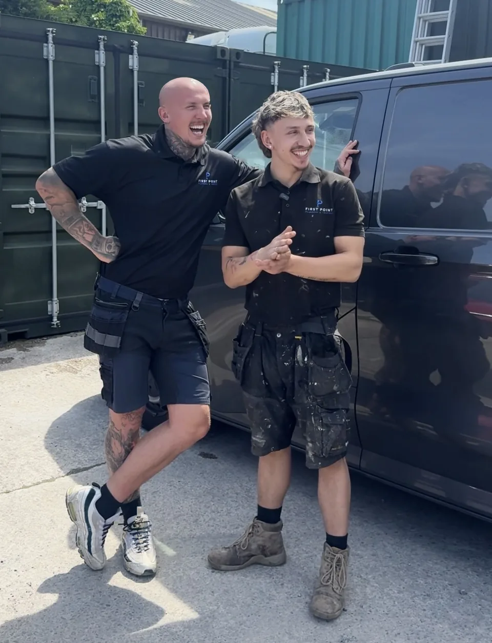 Two First Point engineers in black branded polos laughing beside a dark grey van