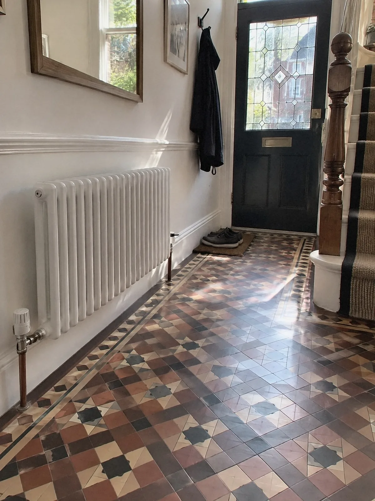 Illustration of a new white column radiator in a Victorian hallway with a patterned tiled floor, the front door and staircase beyond