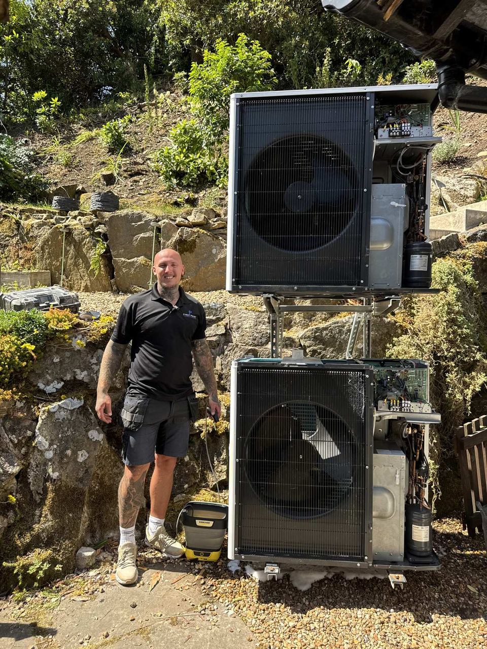 Engineer beside two stacked outdoor heat pump units, side panels off, control boards and compressors exposed