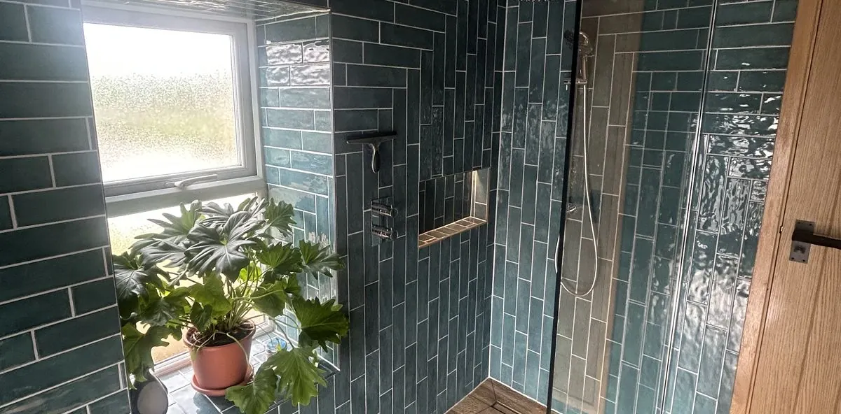 Wet room tiled floor to ceiling in teal gloss metro tile, with a frameless glass screen, a chrome rain head and a plant on the tiled window sill